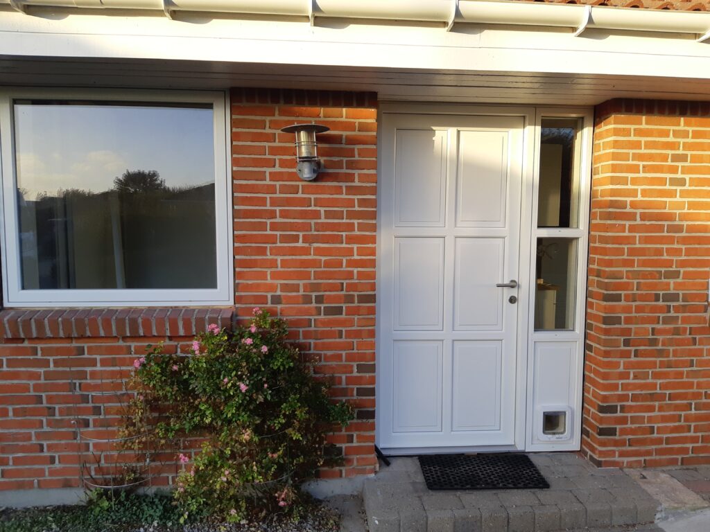 Hvid hoveddør i plast i murstenshus med vindue og kattelem