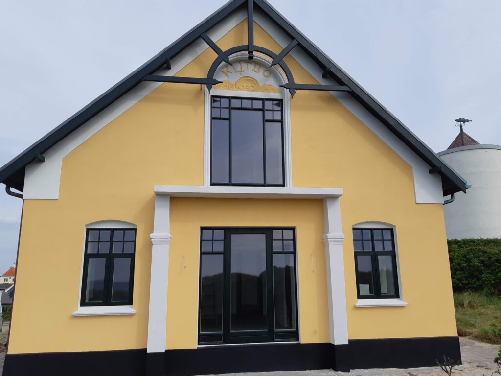 Gul bygning med sorte vinduer i plast og hvide detaljer