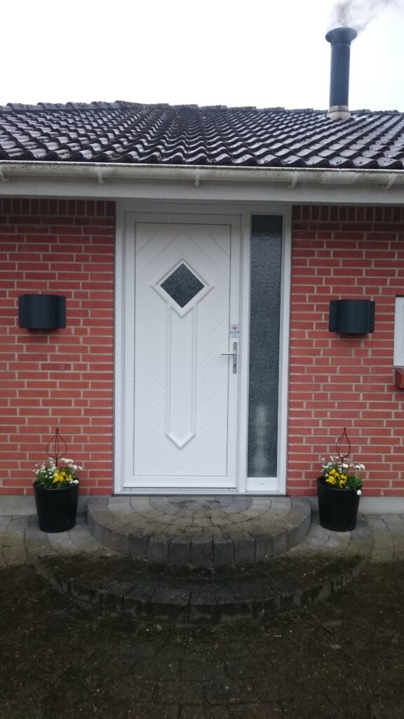 Hvid hoveddør i plast i murstenshus med blomsterkrukker