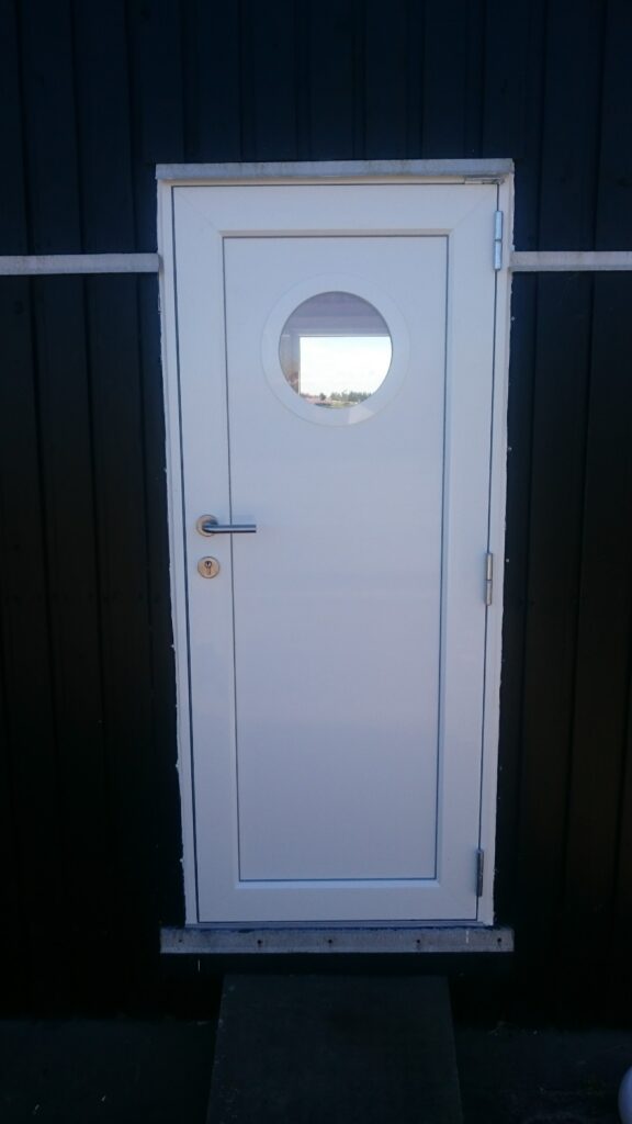 Hvid plastdør med rundt vindue på mørk væg