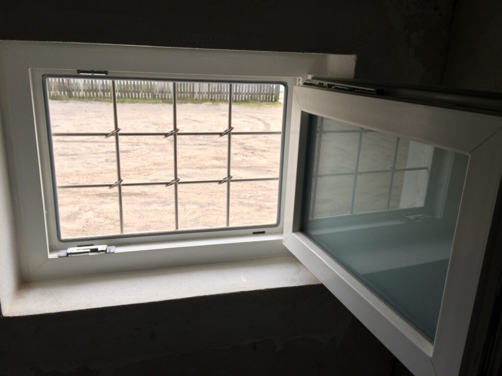 Åbent kældervindue med metalgitter og gårdsplads udenfor